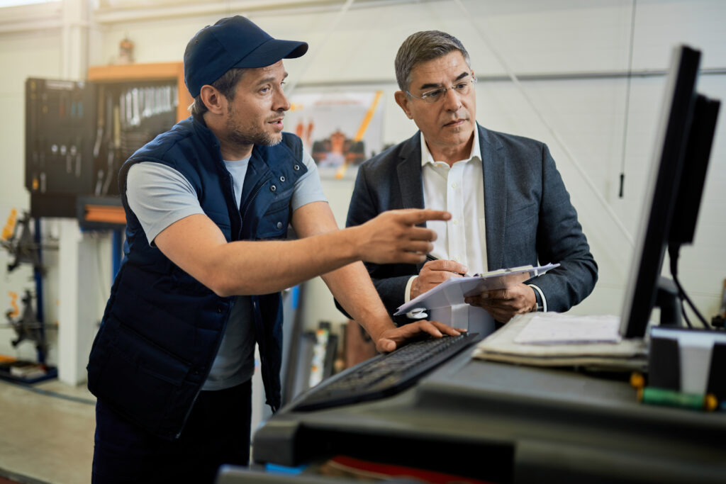 mid adult manager car mechanic talking while using computer auto repair shop
